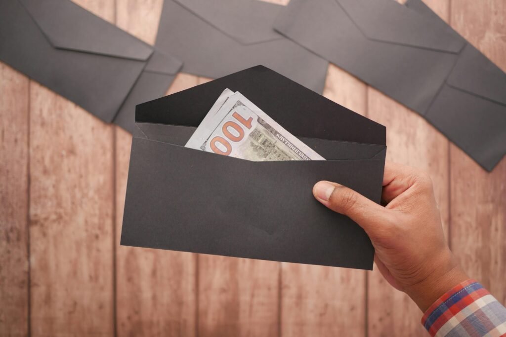 A hand holds a black envelope containing a 100 dollar bill on a wooden surface.