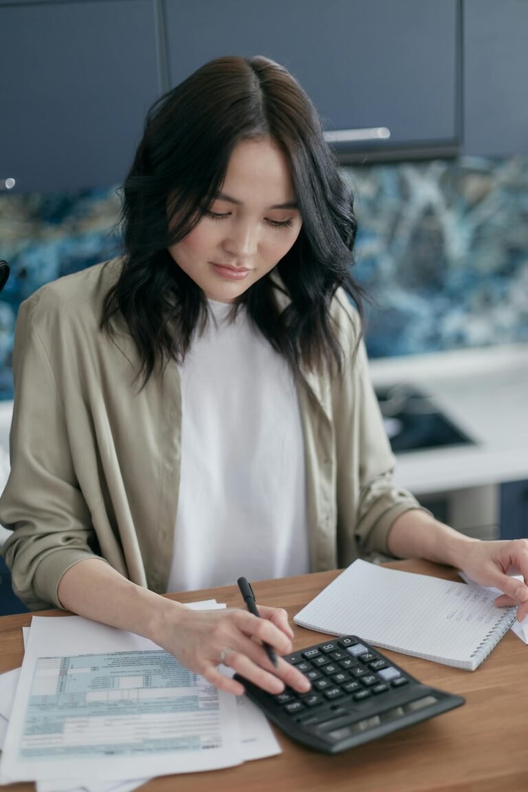 Woman using a calculator for budgeting and finance management at home desk.
