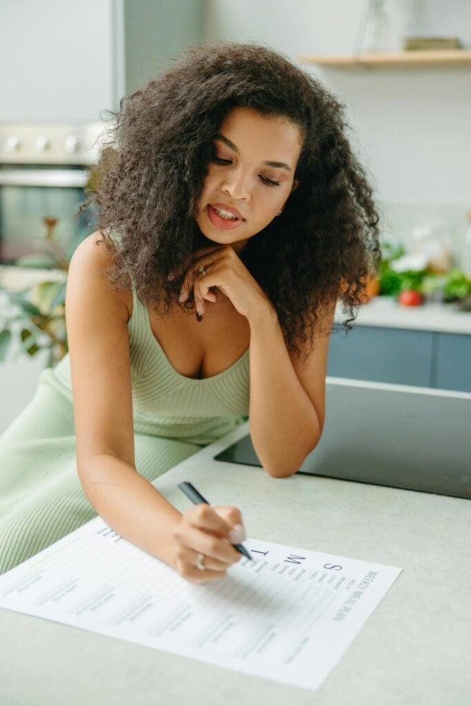 Young woman with curly hair planning a healthy meal indoors. Focus on meal planning and lifestyle.