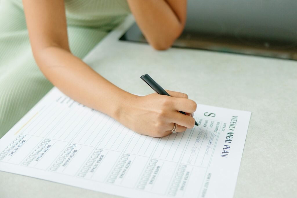 Close-up of a woman writing a weekly meal plan at home, promoting a healthy lifestyle.