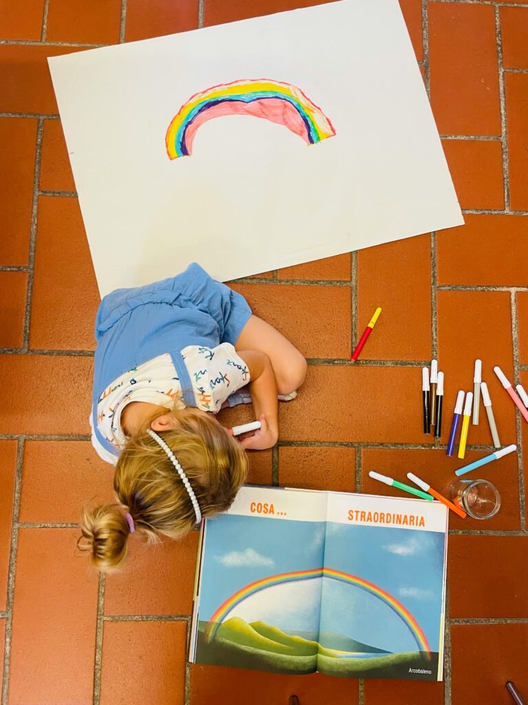 Little girl draws a vivid rainbow on paper with markers, inspired by a book picture.