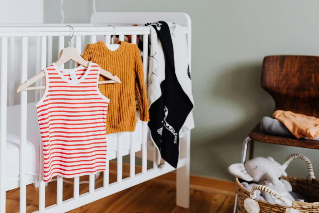 A warm-toned baby room featuring a crib, clothes, and stuffed toy creating a cozy ambiance.